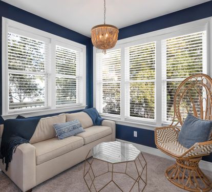 Unwind in your stylish living room with rich navy walls, cozy seating, and a unique wicker peacock chair that's perfect for curling up with a book.