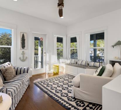 Relax in your bright coastal living room with nautical touches, built-in window seating, and views of lush greenery.