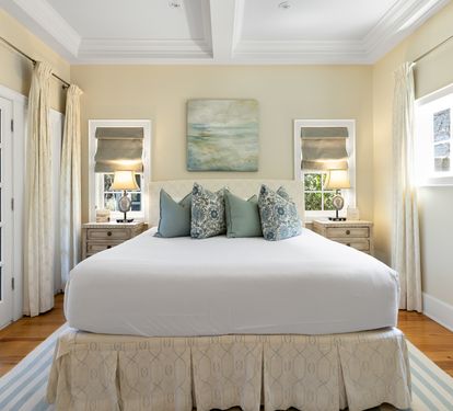 Drift into peaceful sleep on this plush bed, surrounded by warm coastal colors and soft natural light from French doors.