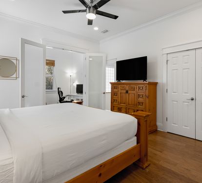 Unwind in your serene bedroom featuring crisp white linens, warm wood floors, and thoughtful touches like a ceiling fan for comfort.