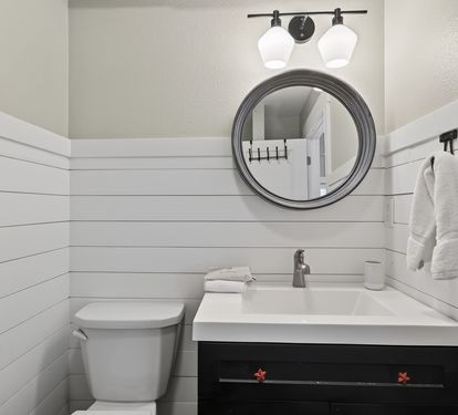 Your pristine powder room features modern farmhouse charm with crisp white shiplap walls, elegant lighting, and thoughtful amenities.