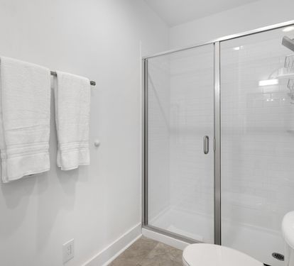 Step into your pristine bathroom featuring a spacious glass-enclosed shower with modern fixtures and fresh towels awaiting your arrival.