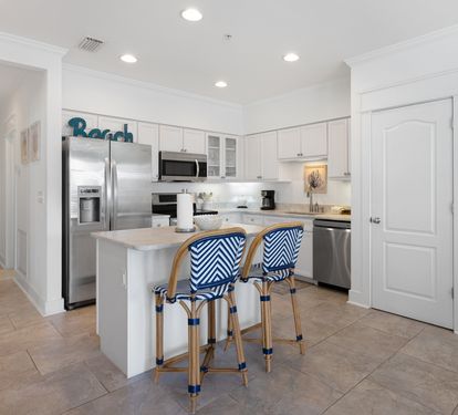 Your coastal-inspired kitchen awaits with crisp white cabinets, stainless appliances, and stylish blue-striped stools perfect for morning coffee.