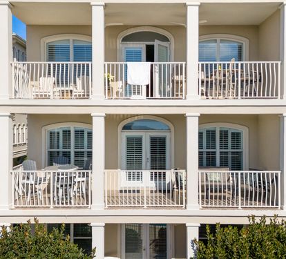 Elegant coastal architecture featuring multiple private balconies with white railings and arched windows in a peaceful beachside setting.