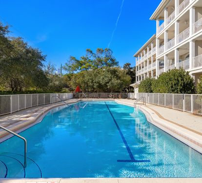 A crystal-clear pool awaits your perfect vacation day, surrounded by lush trees and bright blue skies.