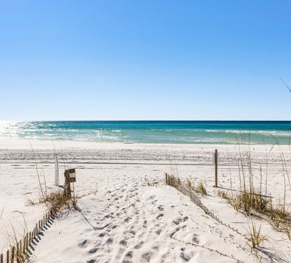 Pristine white sand beach with turquoise waters and dunes, featuring a scenic boardwalk path to the shoreline.