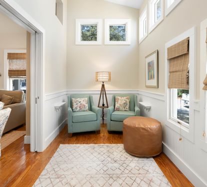 Your peaceful reading nook awaits with twin seafoam chairs, warm leather ottoman, and natural light streaming through bamboo shades.