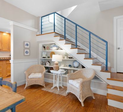 Your charming living space features nautical touches and cozy wicker seating beneath sleek stairs, perfect for morning coffee or evening relaxation.