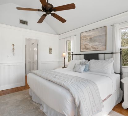Unwind in your peaceful bedroom featuring crisp white linens, warm wood floors, and a gentle ceiling fan overhead.