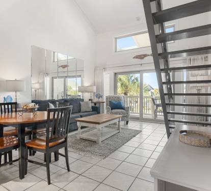 Your bright coastal retreat features an open-plan living space with ocean-inspired decor, comfortable seating, and large windows flooding the room with natural light.