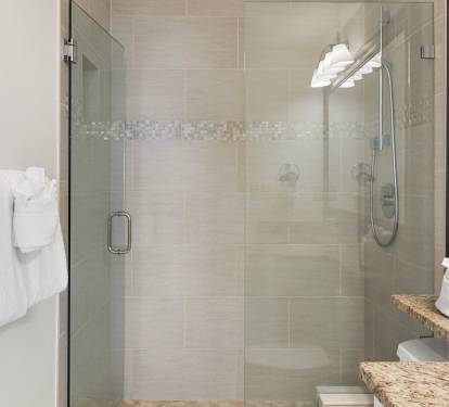 Step into your spa-like bathroom featuring a spacious glass shower with elegant mosaic tile details and plush towels ready for your stay.
