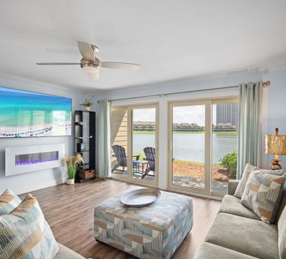 Bright lakefront living room with sliding glass doors, modern fireplace, cozy sectional, and LVP wood floors. Relaxed, coastal vibe with patio access and scenic views.