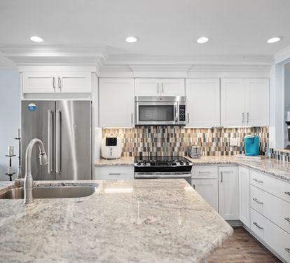 Sleek kitchen with granite countertops, stainless steel appliances, white cabinetry, and a bold tile backsplash. Bright, modern, and fully equipped for cooking and entertaining.