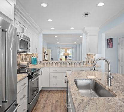 Contemporary kitchen with granite countertops, stainless steel appliances, white cabinetry, and a stylish backsplash. Features an open layout with bar seating.