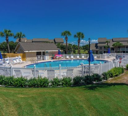 Resort-style pool area with lounge chairs, umbrellas and palm trees, perfect for sunny, relaxing days.