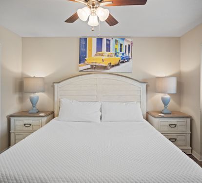 Cozy primary bedroom with a king bed, matching nightstands, and soft lighting from bedside lamps. Features a ceiling fan, neutral walls, and vibrant artwork for a warm, inviting atmosphere.