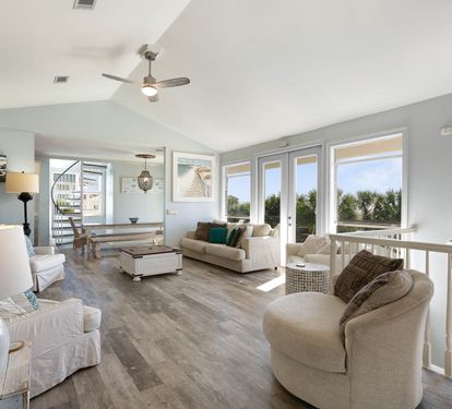 Relax in your bright, coastal-inspired living space with panoramic windows framing tropical views and comfortable seating perfect for unwinding.