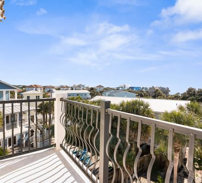 Private balcony with decorative railings overlooking coastal neighborhood homes and palm trees under bright blue skies.