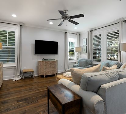 Sink into plush seating in your bright living space, where natural light flows through shuttered windows and coastal decor creates a serene retreat.