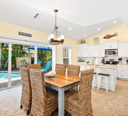 Open-concept kitchen and dining area at Coastal Cottage in Holmes Beach on Anna Maria Island. The fully equipped kitchen features stainless steel appliances, a breakfast bar, and generous counter space, flowing into a dining space that seats six. Sliding 