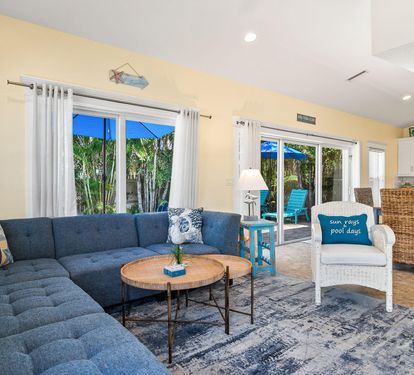 The open living room offers comfortable sectional seating, sliding doors out to the patio, and a bright, coastal-inspired palette throughout.