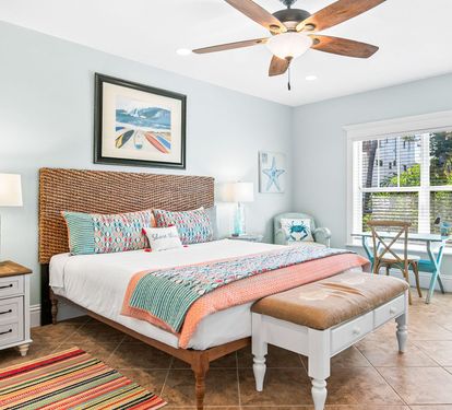 A calm, coastal-toned bedroom with a woven headboard and comfortable queen bed, freshly dressed in new linens.