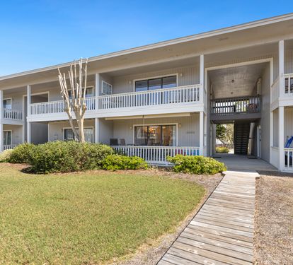 Charming two-story building with white railings and walkway, surrounded by manicured lawns and landscaping under clear blue skies.