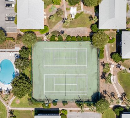 Aerial view shows property complex with tennis courts, swimming pool, and landscaped grounds surrounded by residential neighborhood.