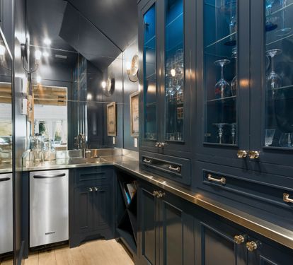 Step into your elegant butler's pantry with custom navy cabinetry, gleaming brass fixtures, and glass displays for your entertaining essentials.
