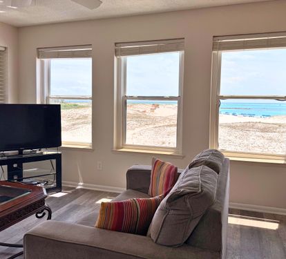 Wake up to panoramic ocean views through expansive windows framing turquoise waters and sandy shores. Relax in your comfortable living space while watching waves roll in just steps away.