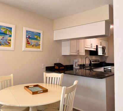 Your bright, fully equipped kitchen opens to a cozy dining nook where beachy artwork sets a relaxed, coastal mood for meals together.