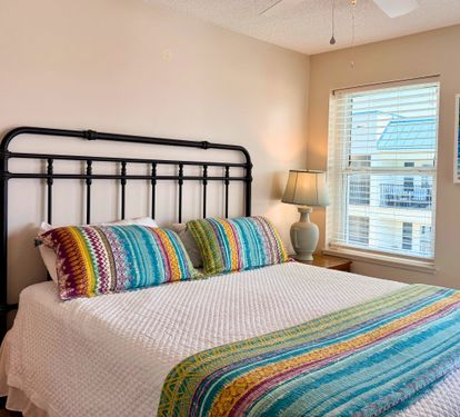 Your primary bedroom retreat features a comfy bed dressed in vibrant linens, soft natural light, and cheerful coastal artwork to start your mornings peacefully.