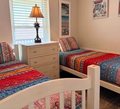 Unwind in your coastal-inspired guest bedroom featuring two twin beds with vibrant bohemian quilts, a charming bedside lamp, and beachy artwork that'll transport you to paradise.