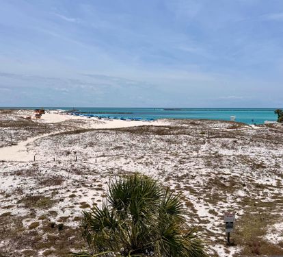 A coastal property location features sandy terrain, native vegetation, and stunning turquoise waters visible from the surrounding area.