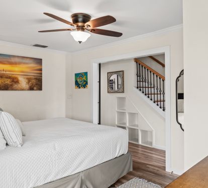 Unwind in your coastal-themed bedroom featuring crisp white linens, a cooling ceiling fan, and charming beach artwork that sets the perfect vacation mood.