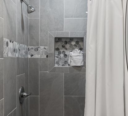 Step into your sleek tiled shower featuring modern gray tiles, hexagon accent details, and a convenient built-in niche for your toiletries.