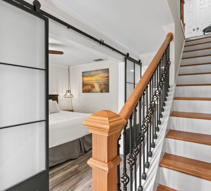 Elegant wooden stairs lead to your private bedroom loft, where modern barn doors create intimate separation while preserving the open, airy feel.