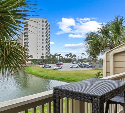 Waterfront property balcony overlooking a tropical canal with palm trees and coastal high-rise buildings visible across the water.