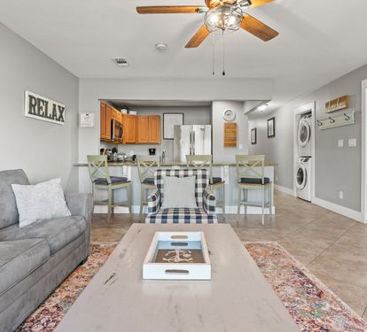 Open living space with coastal décor, comfortable seating, and a full kitchen designed for easy vacation living.