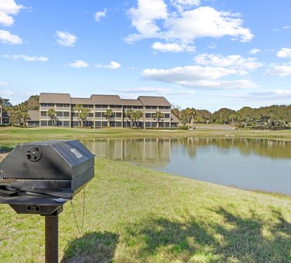 Community charcoal grilling area with peaceful golf course and lake views—perfect for outdoor meals after a beach day.