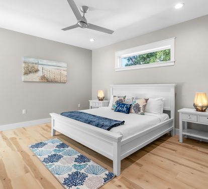 Drift off to peaceful sleep in your serene bedroom, featuring warm wood floors, coastal artwork, and gentle ceiling fan breezes.
