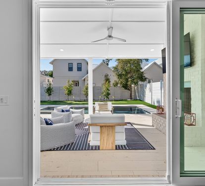 Your modern patio flows seamlessly outdoors through glass doors, revealing designer seating and a sparkling pool beyond.