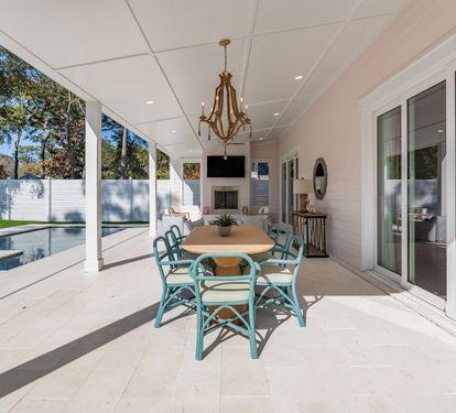Your elegant covered patio awaits with poolside dining, complete with turquoise chairs and a sparkling chandelier overhead.