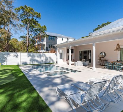 Modern property featuring pristine pool area, covered patio with dining space, and lush landscaping under clear blue skies.