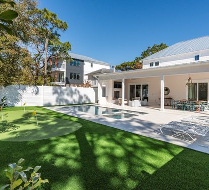 Modern vacation rental with swimming pool and covered patio area surrounded by lush landscaping and mature trees.