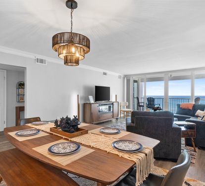 Your stylish oceanfront retreat features an open-plan living and dining space where warm wood accents meet stunning sea views through floor-to-ceiling windows.