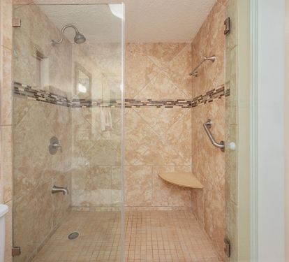 Step into your spacious walk-in shower with elegant travertine tiles, rainfall head, and convenient built-in seating for ultimate comfort.