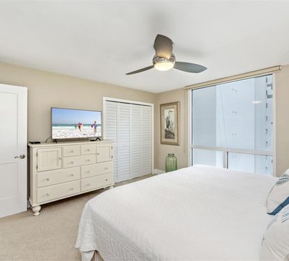Your peaceful bedroom sanctuary features coastal charm with white furnishings, a ceiling fan for comfort, and large windows filling the space with natural light.