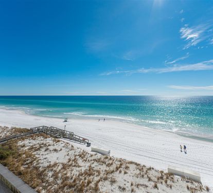 Pristine white sand beach with turquoise waters and wooden walkway access under brilliant blue skies.