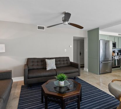 Relax in your spacious living room with modern furniture, ceiling fan, and stylish sage-green kitchen just steps away.